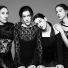 Black-and-white photo of Las Migas in elegant black dresses, posing with serious expressions
