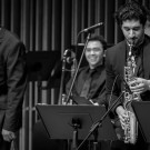 Black-and-white photo of three jazz musicians: two saxophonists and a smiling drummer