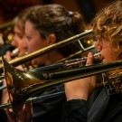 Close-up photograph of trombone players playing gleaming brass instruments