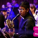Musician playing saxophone horn on purple-lit stage, pink event graphic with the text "Concet happens @ Pitzer Center"