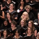 Women's choir in black attire singing from sheet music