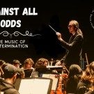 Conductor leads orchestra passionately on dark stage under spotlight, photograph