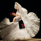 Mexican folkloric dancer in white ruffled skirt mid-twirl, embroidered bodice and red headpiece