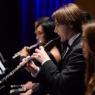 Musicians performing with flutes on stage, dressed in formal black attire.