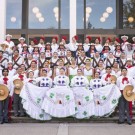 A large group of performers in traditional clothing poses on steps, showcasing vibrant dresses and sombreros.