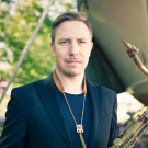 Håkon Kornstad holds a saxophone, standing outdoors near a boat.
