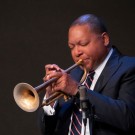 Wynton Marsalis wearing a suit and tie while playing the trumpet.