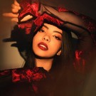 Lucía in a black dress with red accents poses confidently, with dramatic lighting.