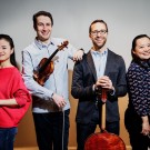 Four smiling string musicians in studio holding violins and a cello
