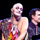 Taylor Mac wears a colorful costume smiles while pianist Matt Ray plays beside them.