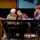 Four actors engaged in a dramatic scene around a wooden table, conveying various emotions.
