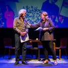 David Suzuki and Tara Cullis facing each other on stage, a colorful projected backdrop and blue stage lighting