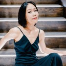 Woman in dark green dress seated on wooden stairs, relaxed posture, direct gaze.