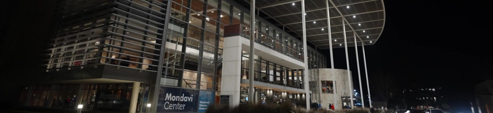 Mondavi Center with large glass windows, illuminated at night, featuring a unique roof design.
