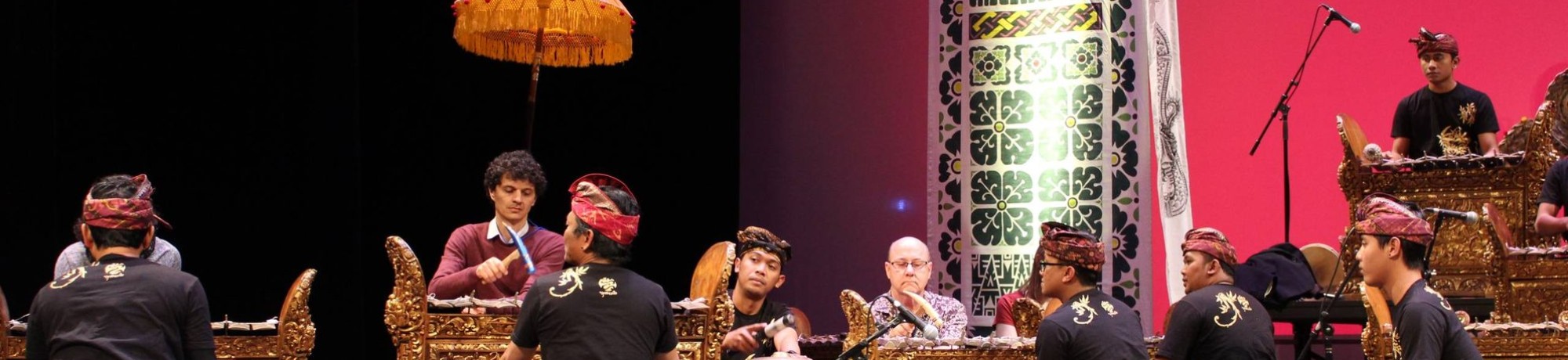 Performers playing traditional instruments on stage with a vibrant pink backdrop.