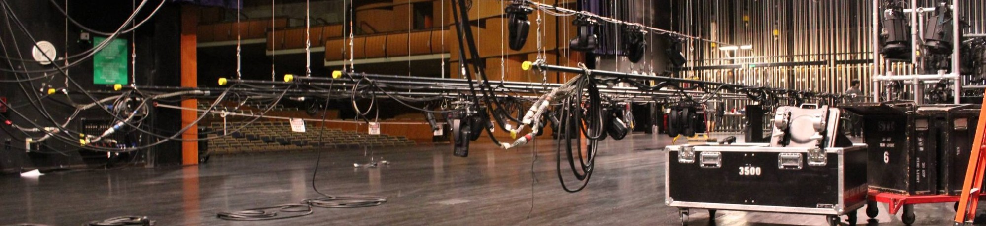 Theater stage with rigging, lighting equipment, and storage crates in a dimly lit setting.