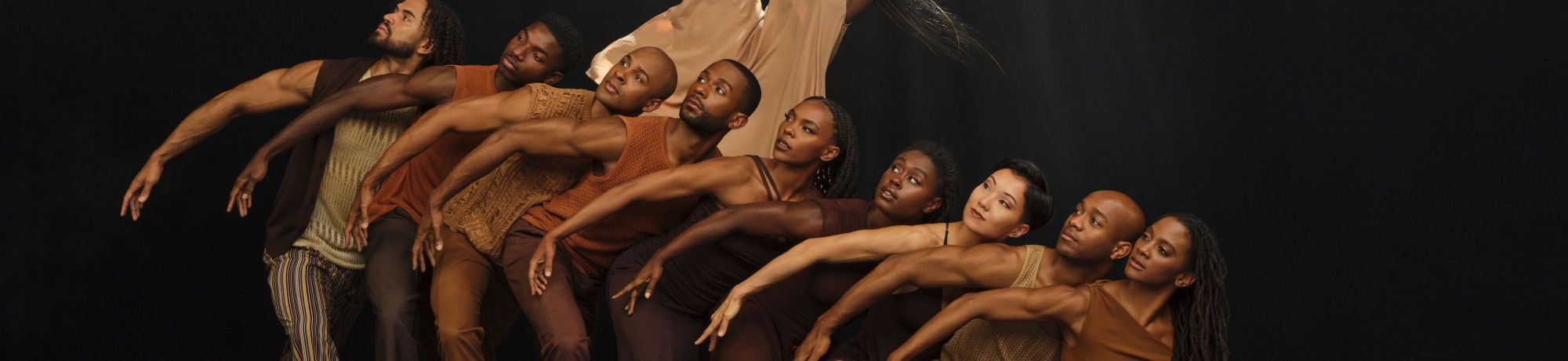 A dynamic group of dancers posed dramatically against a dark background.