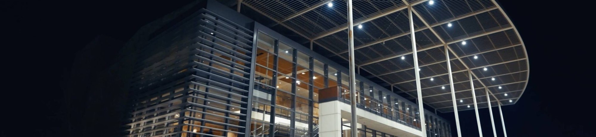 Modern building with a large overhanging roof, illuminated at night.